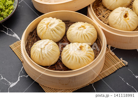 Chinese steamed pork buns (Baozi) inside a traditional bamboo steamer on a dark marble background. 141118991