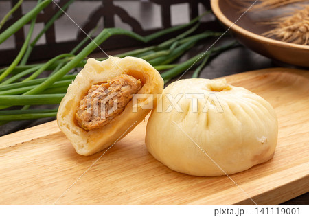Freshly steamed Chinese pork bun cut in half, revealing the savory meat filling on a wooden cutting board. 141119001