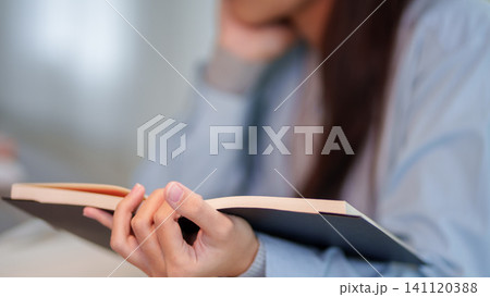 Adult woman holding open book while studying in blurred educational environment with copy space 141120388