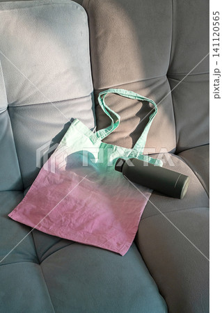 Gradient cotton tote bag with reusable water bottle on gray couch. Gradient cotton tote bag with reusable water bottle on gray couch. 141120565