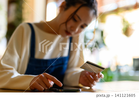 テーブルでスマホとカードを見る女性 テーブルでスマホとカードを見る女性 141121605