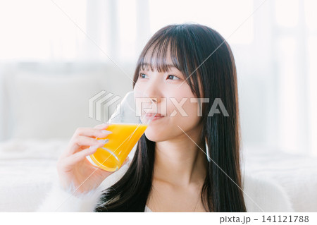 部屋でオレンジジュースを飲む若い女性 部屋でオレンジジュースを飲む若い女性 141121788