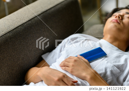 ソファで眠る男性、胸の上にスマートフォンを置く ソファで眠る男性、胸の上にスマートフォンを置く 141121922