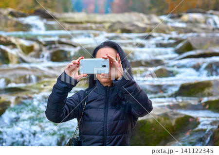 A young woman takes selfie near rocky mountain river with rapid flow A young woman takes selfie near rocky mountain river with rapid flow 141122345