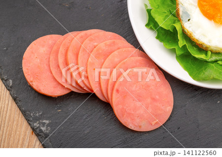 sliced round ham sausage with fresh strawberry and lettuce on black slate 141122560