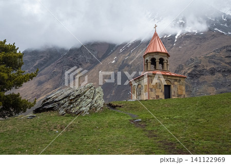 Ancient Stone Bell Tower of Gergeti Trinity Church Against Cloudy Caucasus Mountains in Kazbegi, Georgia Ancient Stone Bell Tower of Gergeti Trinity Church Against Cloudy Caucasus Mountains in Kazbegi, Georgia 141122969