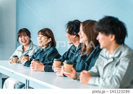 オフィスの休憩所でコーヒーを飲む作業着姿の女性と男性 141123299