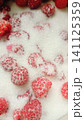 Extreme close-up of vibrant red raspberries scattered on a bed of white granulated sugar, highlighting their texture and seeds. 141125359