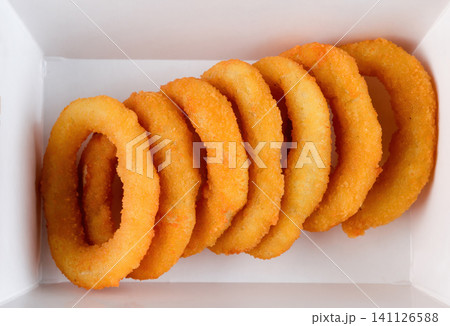 Crispy golden onion ring in white paper takeout container top view extreme close up flat lay delicious savory junk food snack with no background Crispy golden onion ring in white paper takeout container top view extreme close up flat lay delicious savory junk food snack with no background 141126588