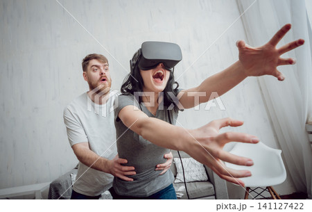 The young man with girlfriend playing games with virtual reality goggles The young man with girlfriend playing games with virtual reality goggles 141127422