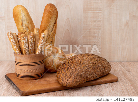 Crispy bread sticks with sesame seeds and bran bread on a wooden board. French baguettes. Different breeds on wooden background. 141127488