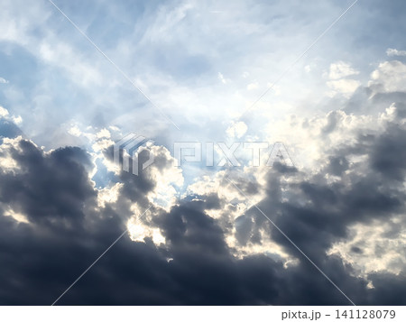 Sunbeams glow behind heavy grey clouds in a dramatic sky. Cloudscape with rays of light breaking through 141128079