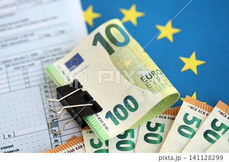 European euro currency money notes bunch on tax form and European union blue flag close up European euro currency money notes bunch on tax form and European union blue flag close up 141128299