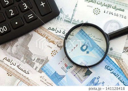 United Arab Emirates dirham currency money bills and calculator with magnifying glass. The concept of taxation and money count United Arab Emirates dirham currency money bills and calculator with magnifying glass. The concept of taxation and money count 141128418