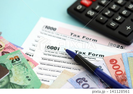 Thai baht money bills and calculator with tax form on blue. Taxation and accounting concept Thai baht money bills and calculator with tax form on blue. Taxation and accounting concept 141128561