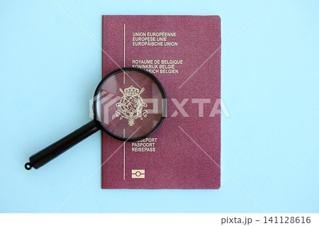 Belgium passport and magnifying glass on light blue paper. Citizenship details and information Belgium passport and magnifying glass on light blue paper. Citizenship details and information 141128616