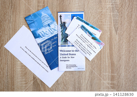 Permanent resident green card in envelope and guide for new immigrants lies on wooden table Permanent resident green card in envelope and guide for new immigrants lies on wooden table 141128630