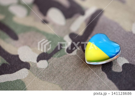 Glass heart with Ukrainian flag lies on military camouflage fabric. Concept of support Ukraine 141128686