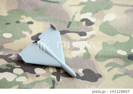 Unnamed grey toy drone model on camouflage fabric. Kamikaze drone for bombing targets Unnamed grey toy drone model on camouflage fabric. Kamikaze drone for bombing targets 141128687