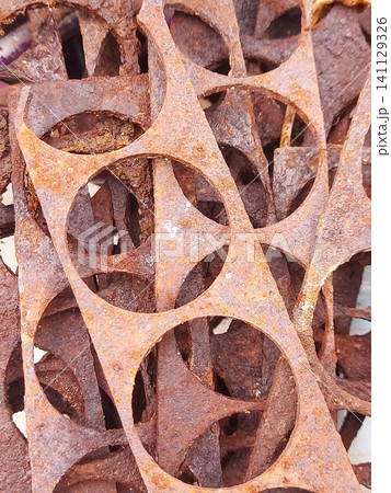 Close-up of rusty metal industrial scraps with circular cutout patterns. Corroded steel texture, abstract geometric shapes, weathered metal background, oxidation, recycling concept, grunge surface 141129326