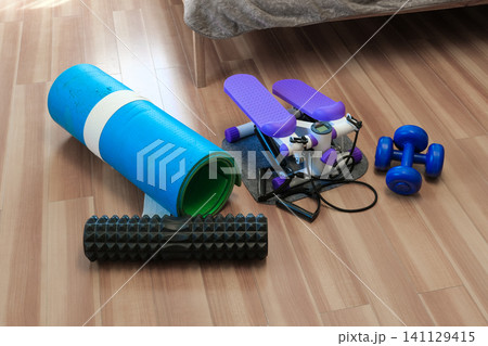 Sport Home exercise equipment. Efficient workout routine. Fitness gear placed for home fit. Yoga mat, roller, dumbbells on room floor ready for recovery session. Personal inventory for weight loss Sport Home exercise equipment. Efficient workout routine. Fitness gear placed for home fit. Yoga mat, roller, dumbbells on room floor ready for recovery session. Personal inventory for weight loss 141129415