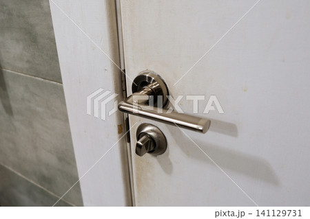 Doorknob. Metal door handle lock and latch of brass on veneer doors. Door wooden half opening through interior bedroom background, selective focus. Modern trends in interior design. Close-up Doorknob. Metal door handle lock and latch of brass on veneer doors. Door wooden half opening through interior bedroom background, selective focus. Modern trends in interior design. Close-up 141129731