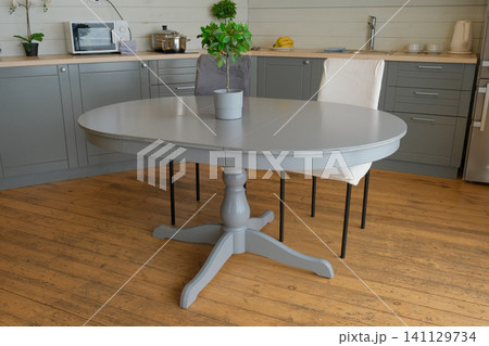 Dining room interior. Gray oval dining table, wood flooring, grey cabinets. Interior design of stylish kitchen with family table, modern chairs. Wooden floor. White wall. Template. New Luxury Home. 141129734