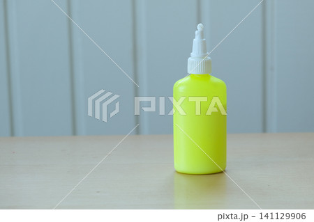 Yellow glue bottle. Bright colored adhesive container on table. Vibrant neon tone bottle with soft shadows. Minimalist image of craft supply ideal for hobby and repair. Copy space, back to school Yellow glue bottle. Bright colored adhesive container on table. Vibrant neon tone bottle with soft shadows. Minimalist image of craft supply ideal for hobby and repair. Copy space, back to school 141129906