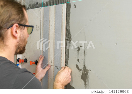 Worker Laying Ceramic Tiles on the Wall. Repairman Placing White Gray Square Tiles, Applying Adhesive. Builder Installing Tile Using Leveler, Tile Leveling Clips. Tiling. Finishing Repair Work. 4K Worker Laying Ceramic Tiles on the Wall. Repairman Placing White Gray Square Tiles, Applying Adhesive. Builder Installing Tile Using Leveler, Tile Leveling Clips. Tiling. Finishing Repair Work. 4K 141129968