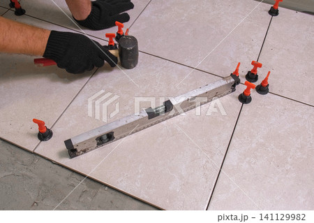 Worker Hand Laying Ceramic Tiles on the Floor. Repairman Placing White Gray Square Tiles, Applying Adhesive. Builder Installing Tile Using Leveler, Tile Leveling Clips. Tiling. Finishing Repair Work. 141129982
