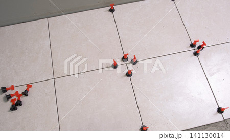Worker Hand Laying Ceramic Tiles on the Floor. Repairman Placing White Gray Square Tiles, Applying Adhesive. Builder Installing Tile Using Leveler, Tile Leveling Clips. Tiling. Finishing Repair Work. 141130014