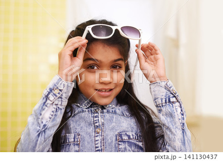 Girl, portrait and sunglasses for home, holiday and vacation with fashion and cool style. Happy face of a young Mexican kid or child with smile, casual and trendy accessory or shades for fun indoors 141130437