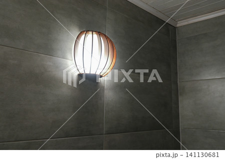 Bathroom wall lamp. Stylish glass sconces with wooden elements hanging on a grey tile wall at home. Modern lighting fixture. Electricity. House, hotel design. Minimalist luminaire casting soft light Bathroom wall lamp. Stylish glass sconces with wooden elements hanging on a grey tile wall at home. Modern lighting fixture. Electricity. House, hotel design. Minimalist luminaire casting soft light 141130681