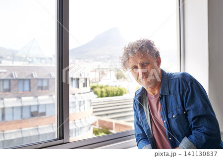 Man, smile and portrait with window in city for relax with view and building for urban and break in house. Mature person and leaning for comfort indoor for peace and alone with mountain and sun flare 141130837