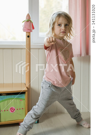 Little 5 years old kid girl practicing punches, karate, taekwondo movements at home. Athlete child practicing martial arts outdoors. Training in autumn day. Nature background. Dynamic Kyungkido. Little 5 years old kid girl practicing punches, karate, taekwondo movements at home. Athlete child practicing martial arts outdoors. Training in autumn day. Nature background. Dynamic Kyungkido. 141131020