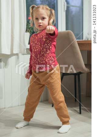 Little 5 years old kid girl practicing punches, karate, taekwondo movements at home. Athlete child practicing martial arts outdoors. Training in autumn day. Nature background. Dynamic Kyungkido. Little 5 years old kid girl practicing punches, karate, taekwondo movements at home. Athlete child practicing martial arts outdoors. Training in autumn day. Nature background. Dynamic Kyungkido. 141131023