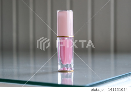 Lipstick on neutral interior background. Liquid lip stick clear tube. Makeup cosmetic product. Front view copy space. Shimmer Pink lip gloss for makeup creating beauty and shine. Glamour modern design Lipstick on neutral interior background. Liquid lip stick clear tube. Makeup cosmetic product. Front view copy space. Shimmer Pink lip gloss for makeup creating beauty and shine. Glamour modern design 141131034