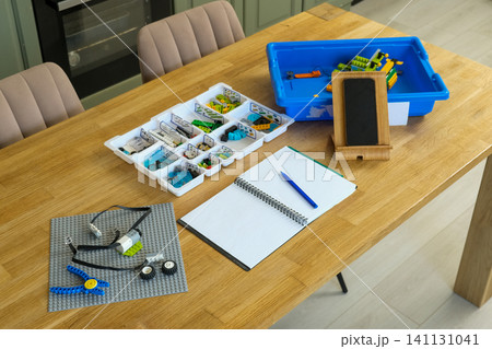 Interactive robotics kit laid out on table, open notebook, tablet, scattered bricks. Kids engineering project scene. Children assembling robotic set on desk. STEM education. Programming electric toys Interactive robotics kit laid out on table, open notebook, tablet, scattered bricks. Kids engineering project scene. Children assembling robotic set on desk. STEM education. Programming electric toys 141131041