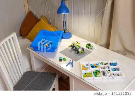 Interactive robotics kit laid out on table, open notebook, tablet, scattered bricks. Kids engineering project scene. Children assembling robotic set on desk. STEM education. Programming electric toys 141131055