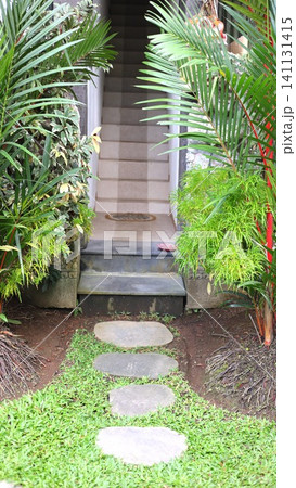 Lush tropical garden path with round stepping stones leading through palm fronds and hanging ferns toward raised tiled stairway entrance beside green lawn, with garden, path, stone, stepping detail Lush tropical garden path with round stepping stones leading through palm fronds and hanging ferns toward raised tiled stairway entrance beside green lawn, with garden, path, stone, stepping detail 141131415