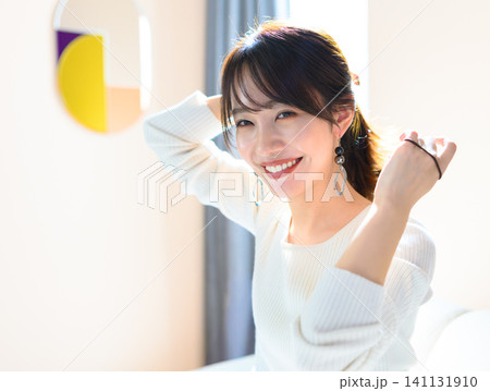 ソファに座って髪を結ぶ若い女性 ソファに座って髪を結ぶ若い女性 141131910