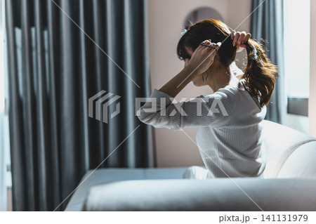 部屋で髪を結ぶ女性 141131979