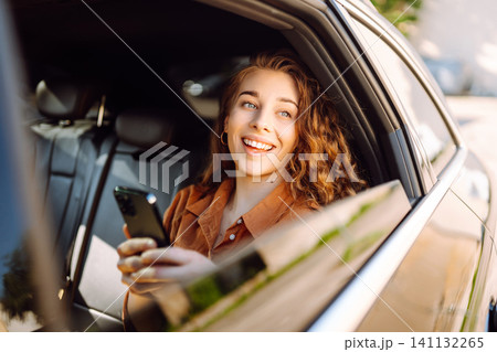 A young woman with a smartphone chats in the back seat of a car. Transport concept. Lifestyle. A young woman with a smartphone chats in the back seat of a car. Transport concept. Lifestyle. 141132265
