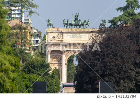 Milan Italy Majestic Triumphal Arch with a Bronze Quadriga Statue, Green Summer Trees. Italian architecture Milan Italy Majestic Triumphal Arch with a Bronze Quadriga Statue, Green Summer Trees. Italian architecture 141132794