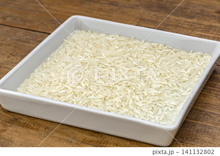 Thai jasmine rice grains in a white square dish, close up view on rustic wooden background, showing white jasmine rice and brown jasmine rice for food ingredient concept 141132802