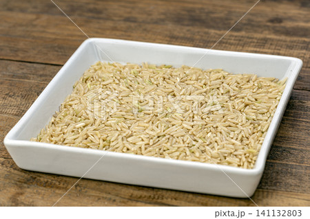 Fragrant Jasmine brown rice grains (jasmine rice, brown rice) in a white ceramic tray on rustic wooden table, close-up food ingredient for healthy diet and cooking Fragrant Jasmine brown rice grains (jasmine rice, brown rice) in a white ceramic tray on rustic wooden table, close-up food ingredient for healthy diet and cooking 141132803