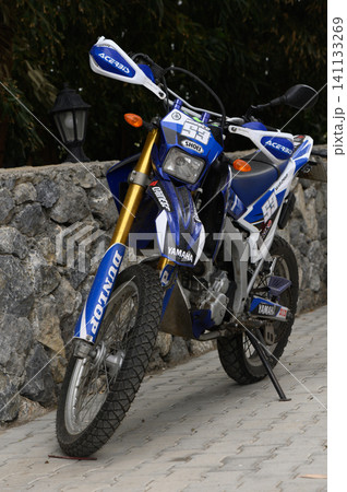 Gaziveren Cyprus -02.04.2025 Stylish blue dirt bike parked beside a stone wall in an outdoor setting during daylight hours Gaziveren Cyprus -02.04.2025 Stylish blue dirt bike parked beside a stone wall in an outdoor setting during daylight hours 141133269