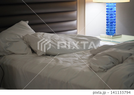 Bed with messy sheets and pillows in hotel room at night Bed with messy sheets and pillows in hotel room at night 141133794