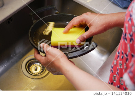 Washing a skillet in the kitchen sink during the afternoon Washing a skillet in the kitchen sink during the afternoon 141134030