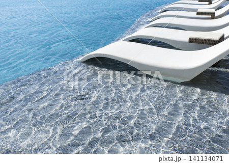 A pool with a white lounge chair on the edge A pool with a white lounge chair on the edge 141134071